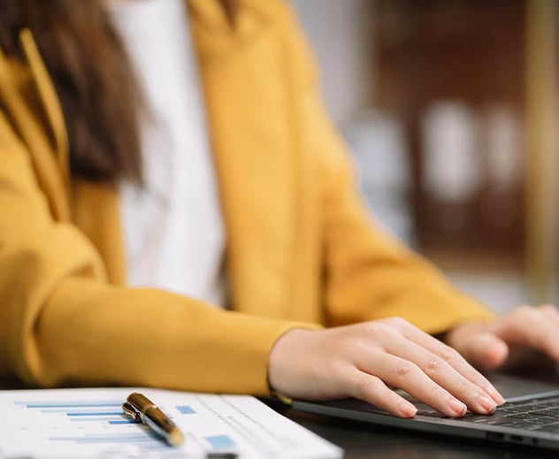 A woman working on a computer and referring to charts.