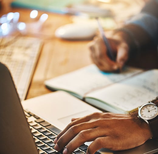 A person taking notes and working on a computer.