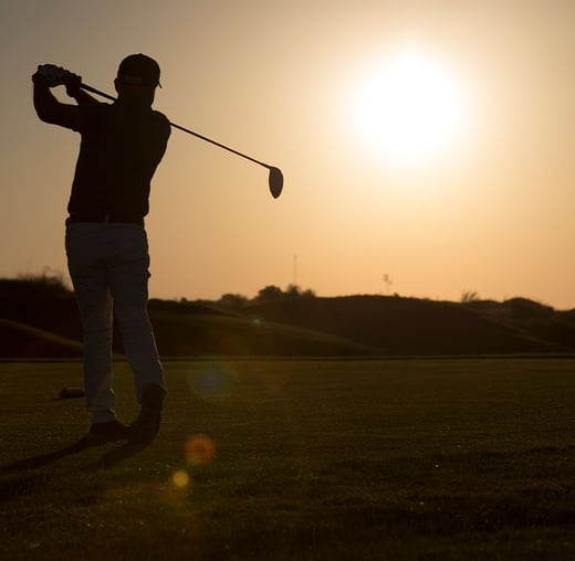A person playing golf as the sun sets.